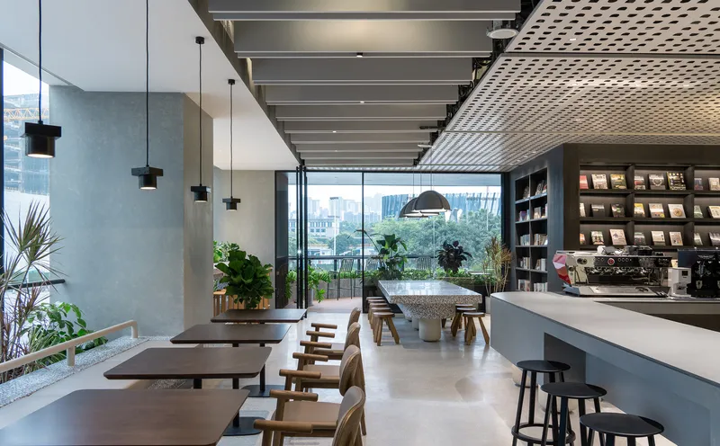 Cafe area with long timber tables, pendant lights, and potted plants framing a view to the terrace