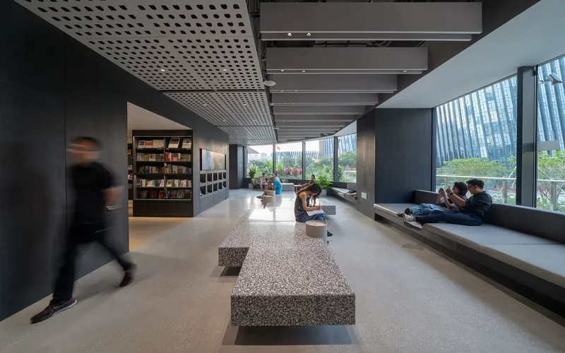 Reading corridor with terrazzo benches, perforated ceiling panels, and visitors seated by the glazed wall