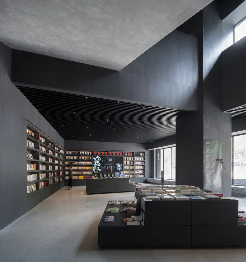 Double-height bookstore volume with ribbed black ceiling, concrete walls, and natural light from clerestory windows