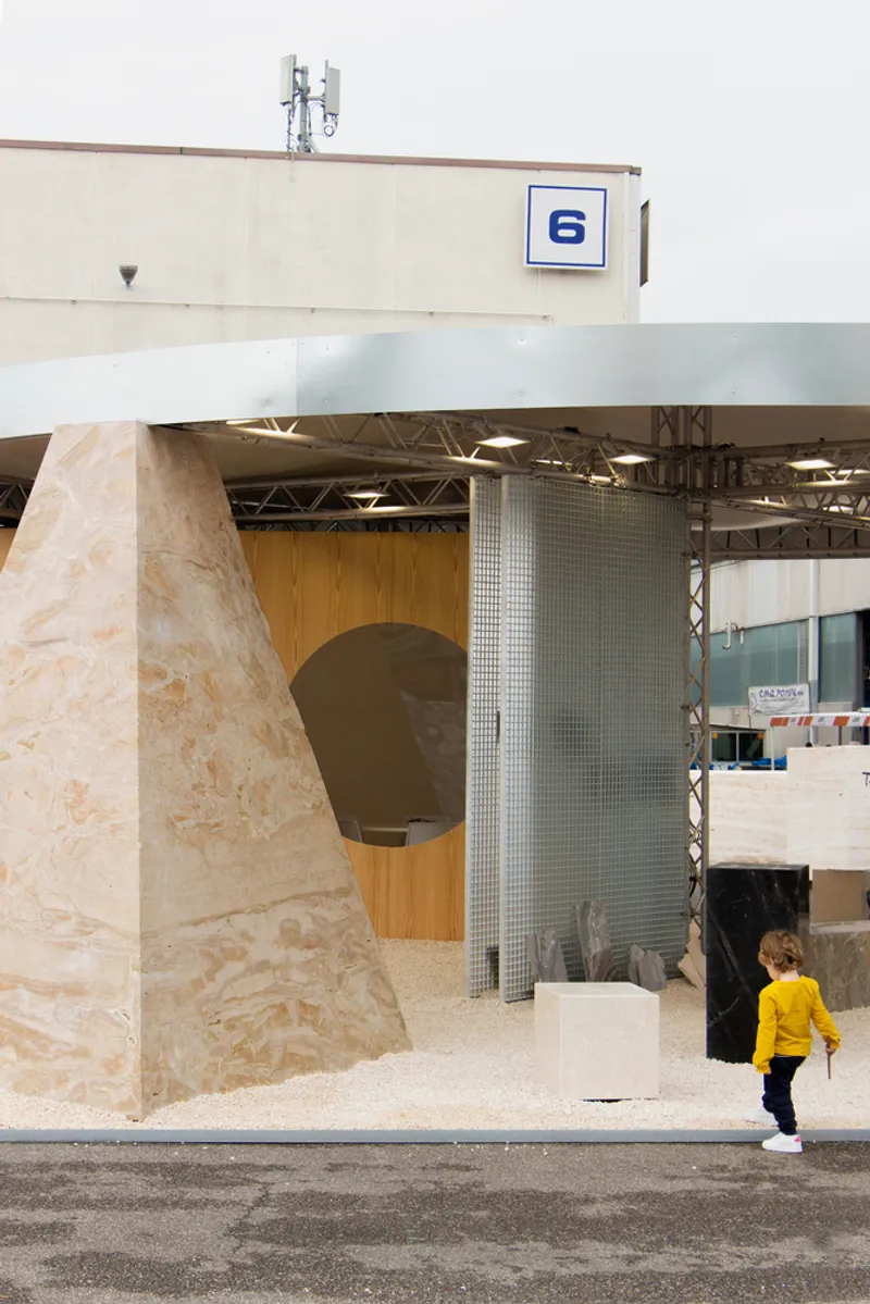 View of the slanted plywood column and glass mosaic wall with child in yellow jacket
