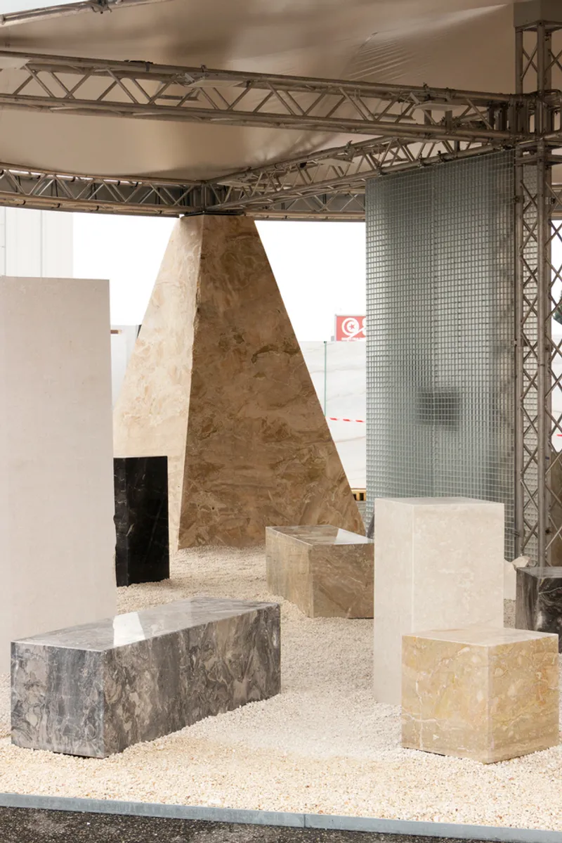 View through plywood columns and white panels with stone samples on gravel floor