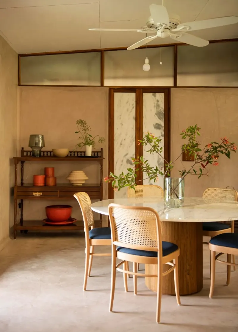A dining room channels a minimalist vibe with a custom table in marble and teak, chairs by ton, and a Bengal shelf by Mahendra Doshi.