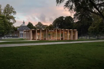 This architectural image showcases a modern pavilion situated in a park setting. The pavilion featur