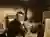 This is a sepia-toned photograph of an artist in his studio, working on a clay sculpture. The artist