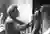 This black and white photograph captures a sculptor in his studio, meticulously working on a clay bu