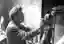 This black and white photograph captures a sculptor in his studio, meticulously working on a clay bu