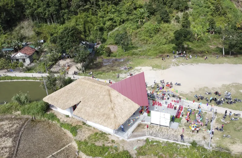 Aerial view of thatched roof pavilion and corrugated metal wing adjacent to terraced rice paddies and hillside dwellings