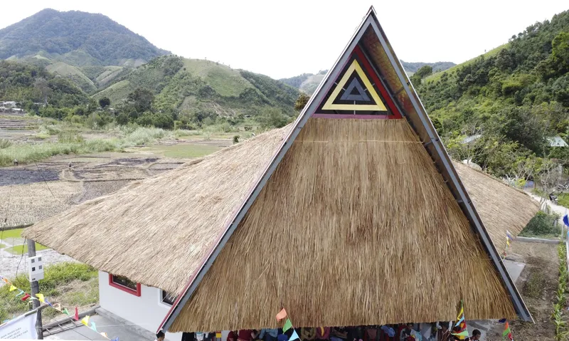 Steep thatched roof with triangular gable decoration set against terraced hillside landscape