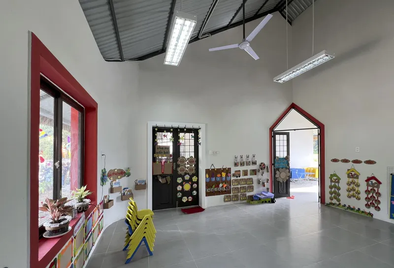 Interior classroom space with exposed corrugated metal ceiling and red-framed doorways and windows