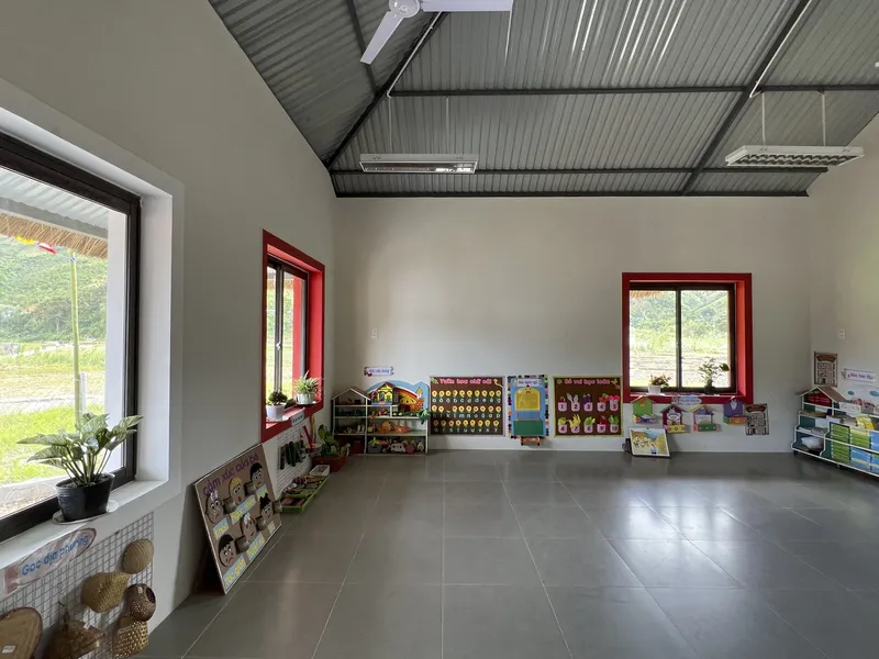 Interior space with red-framed windows along white walls beneath exposed metal truss ceiling