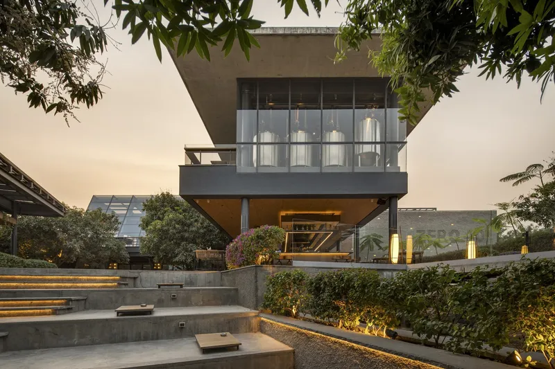Cantilevered concrete upper volume with full-height glazing above a terraced garden at dusk