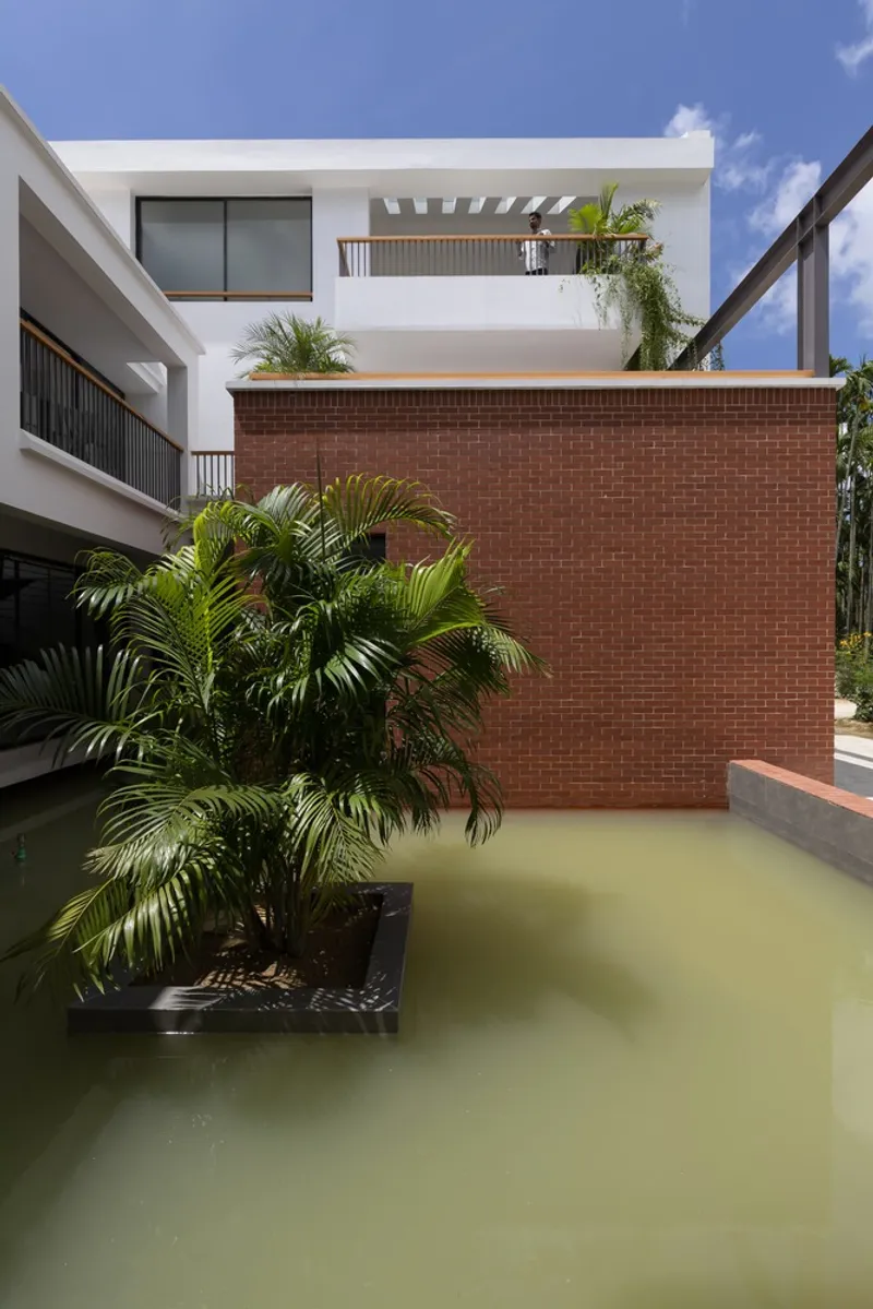 Courtyard water feature with red brick wall and planted palms beneath white residential volumes