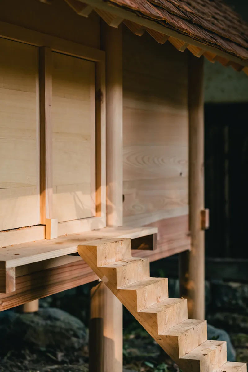 Timber stair ascending to the elevated pavilion with warm light filtering beneath the cedar shingle eaves