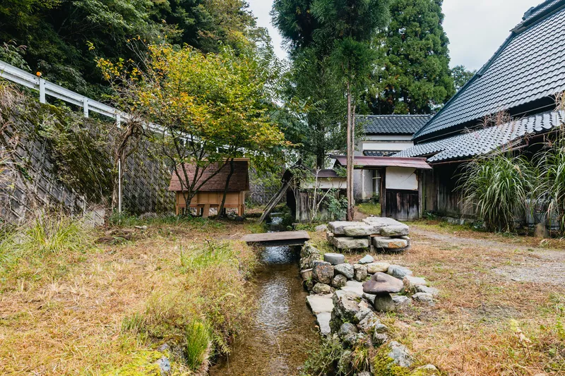Stone water channel with moss and stacked boulders in a courtyard surrounded by tile-roofed buildings