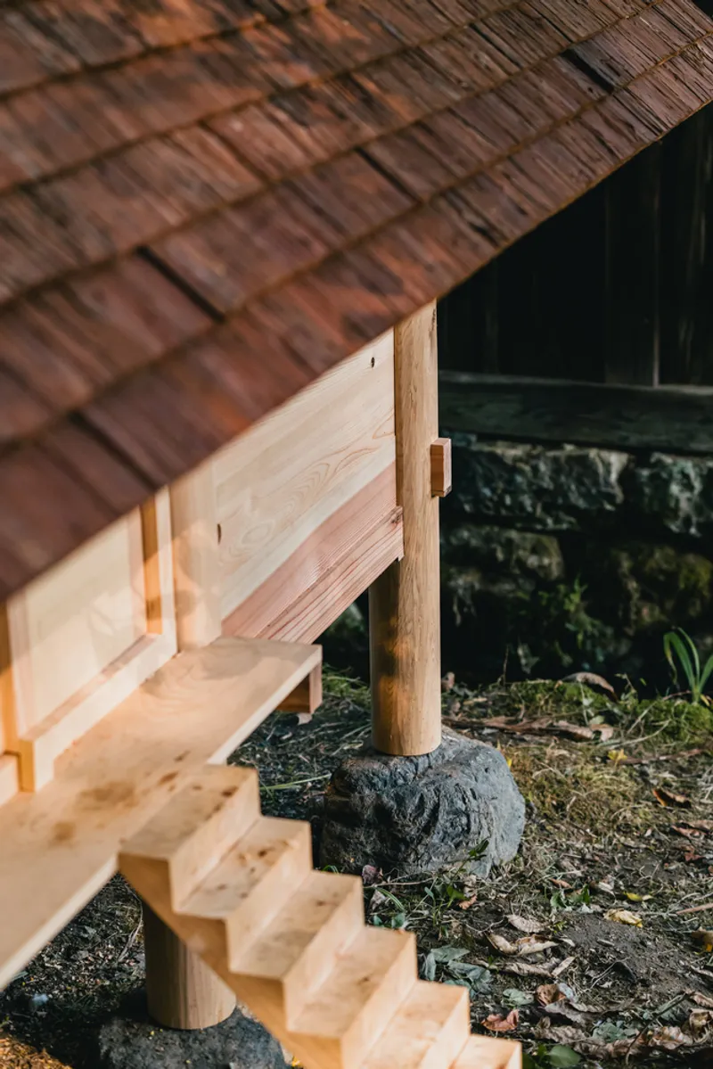 Side view of timber stair and post supporting cedar shingle roof near mossy rocks