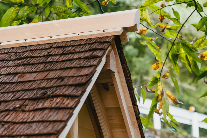 Detail of the timber gable end with cedar shingle roof and exposed rafter tails amid grapevines