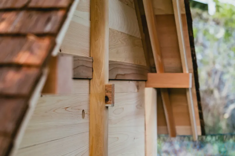 Detail of exposed timber joinery connecting posts and beams beneath shingled roof overhang