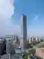 This architectural image showcases a modern skyscraper dominating an urban landscape under a partly 