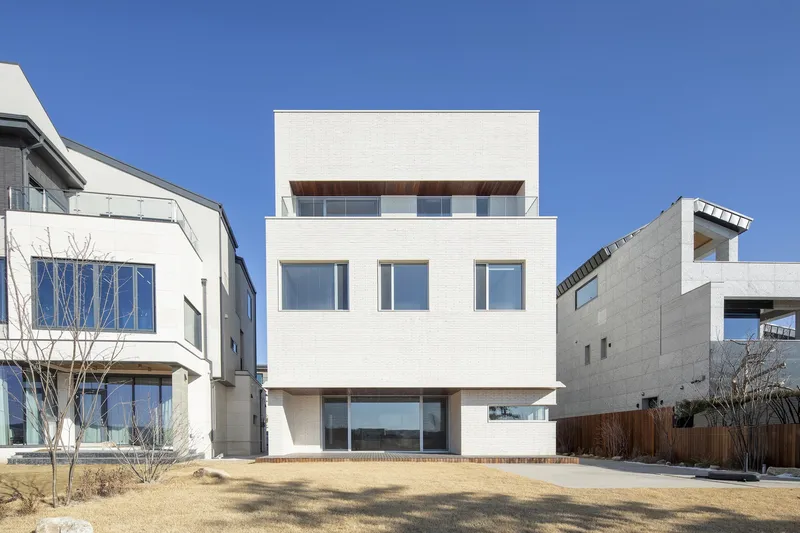 Rear facade of white stacked volumes with timber soffits facing a dormant winter lawn