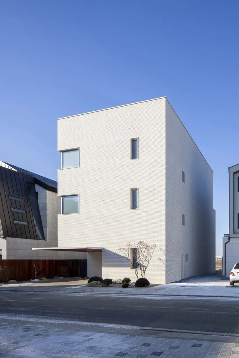 Street view of the white brick facade with asymmetrical punched windows under clear blue sky