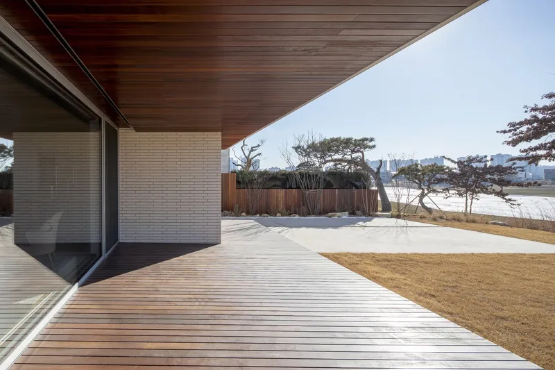 Timber deck terrace with deep eaves overlooking dormant grass and distant pines