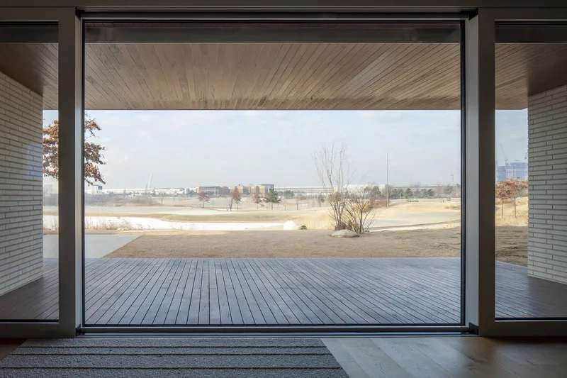 Large glazed opening framing a timber deck terrace and dormant winter field beyond