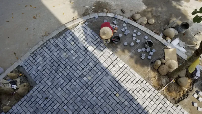 Overhead view of a worker in a straw hat installing mosaic tiles on the courtyard floor