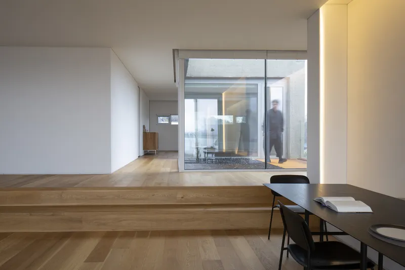 Open interior with timber platform steps overlooking glazed courtyard where a figure walks through