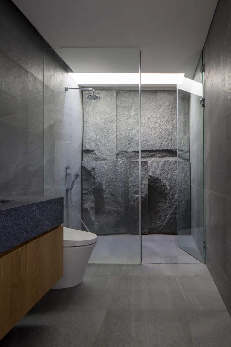 Bathroom with glass shower enclosure revealing textured stone wall and clerestory lighting