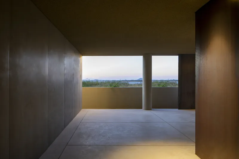 Covered terrace with concrete floor and ceiling framing a horizontal window overlooking distant water and hills