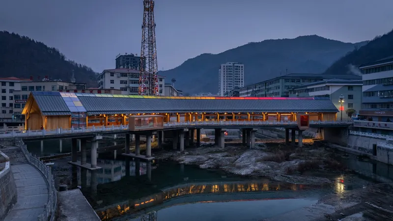 Illuminated bridge deck on concrete piers over a rocky riverbed at dusk with mountains beyond