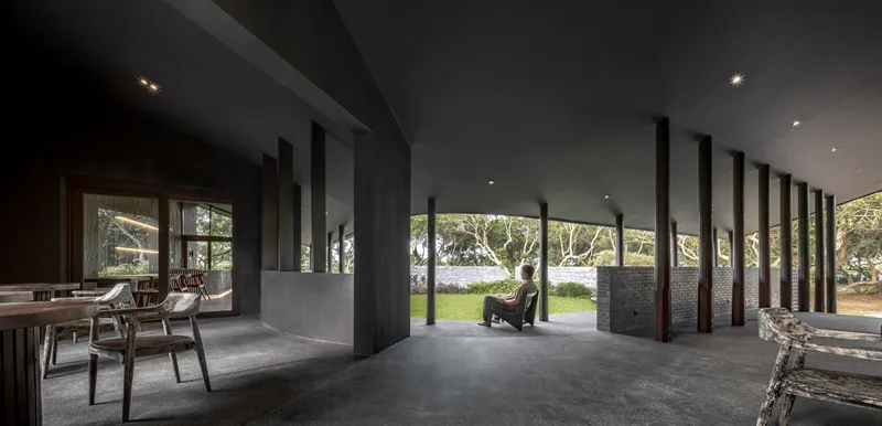Long interior view of the covered terrace with a row of dark columns and a lone seated figure