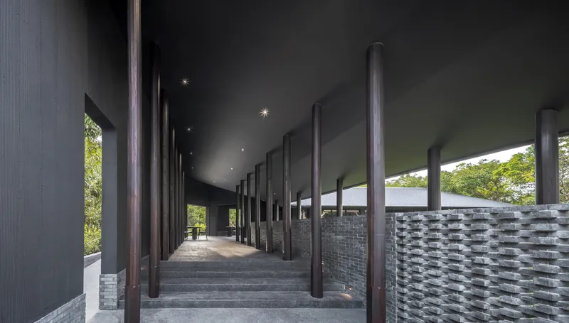 Stepped arrival walkway with tall dark columns and grey brick screen walls