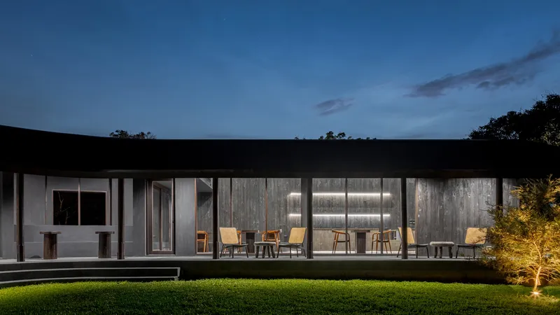 Night elevation of the glazed dining pavilion with timber chairs on the terrace