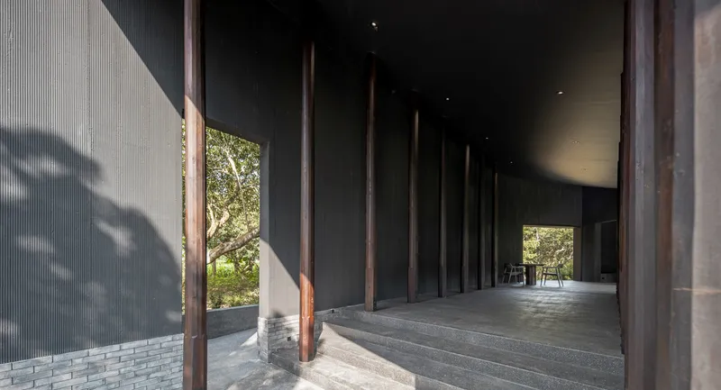 Covered arrival walkway with dark columns and a grey brick wall beneath a curving roof