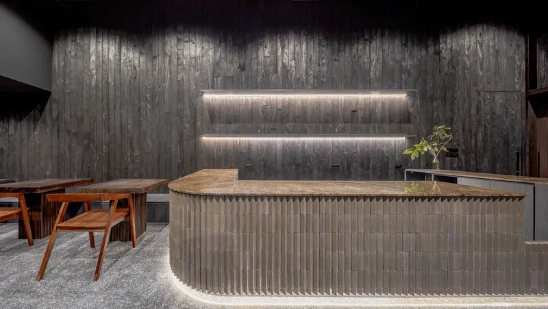 Bar counter detail with a fluted grey brick base and lit niche shelving behind