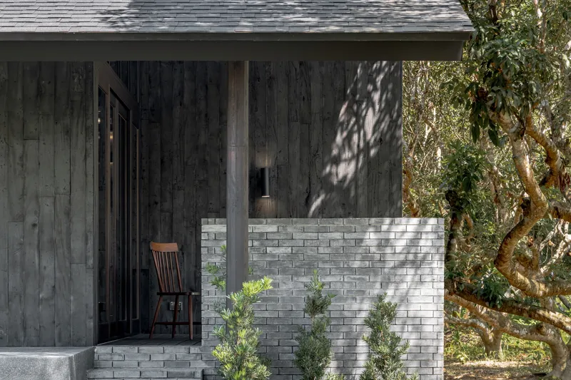 Side entrance porch with a single timber chair and a low grey brick wall