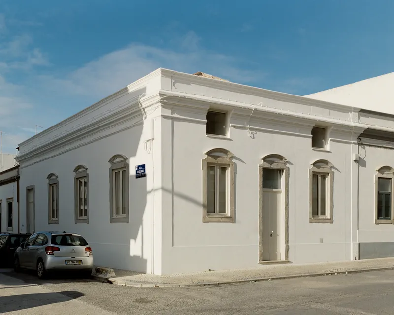 Three-quarter view of the corner house with its restored white stucco facade and arched window architraves