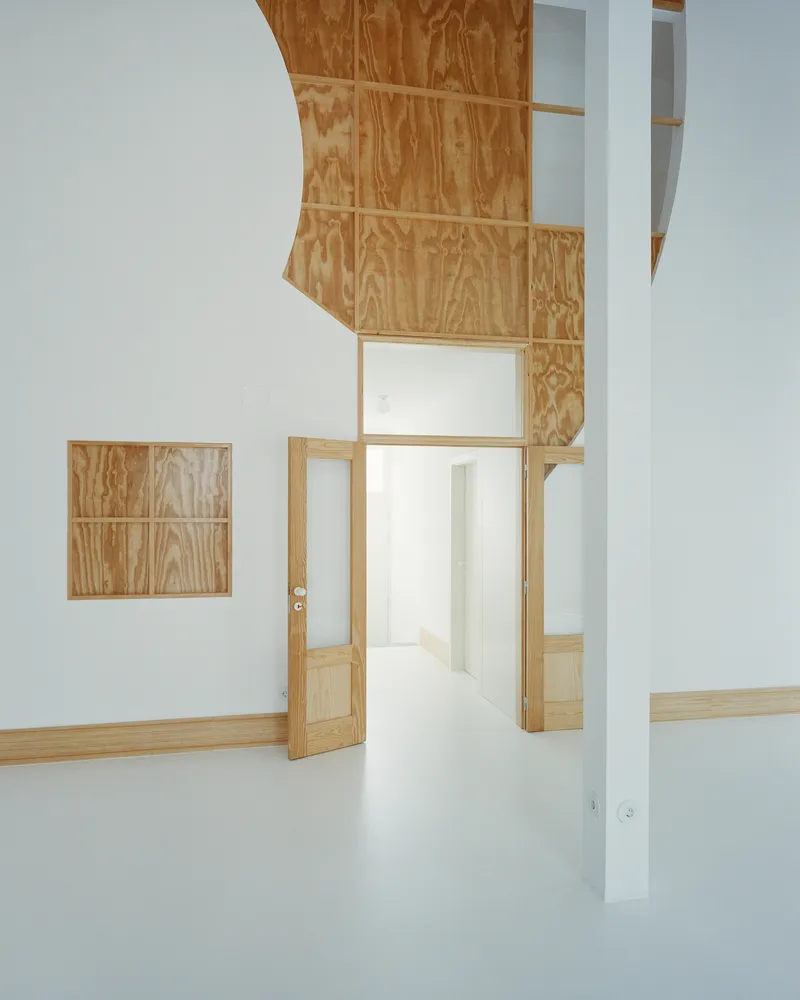 Interior view with a curved plywood-clad ceiling soffit and a thin white pillar dividing the space