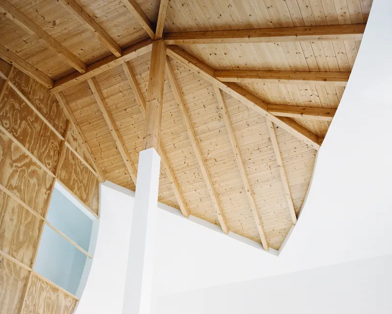Close-up of the pine rafters and the curved plywood wall meeting the white pillar