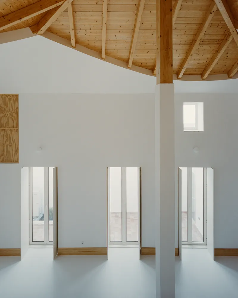 Three full-height window slots on a white wall under the exposed pine roof structure