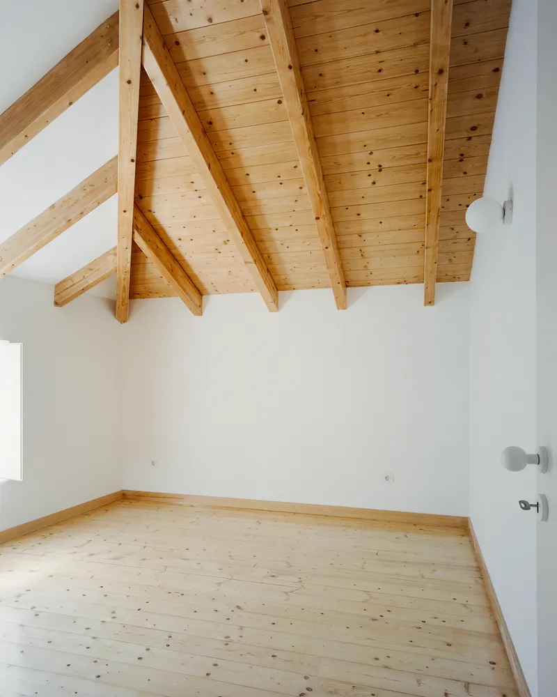 Bedroom under the pine roof with a small window and a timber floor