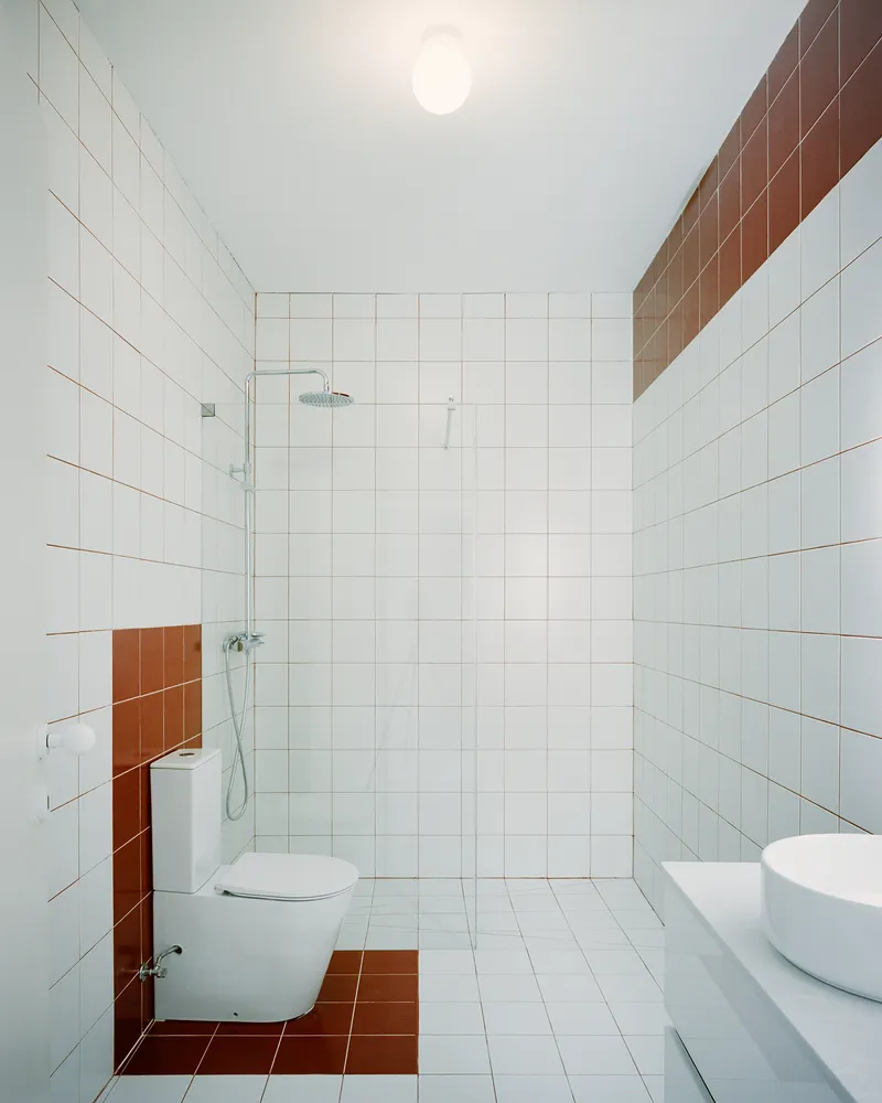 Tiled bathroom with white square tiles and terracotta accents around the toilet and shower