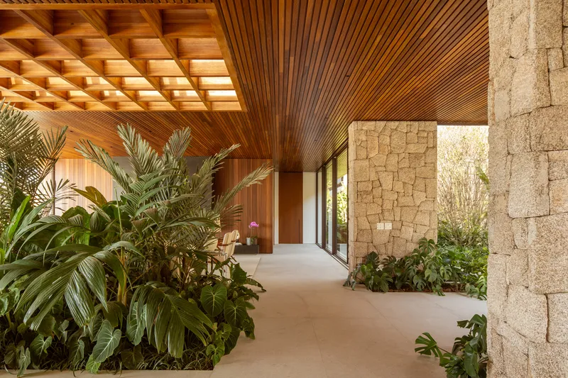 Internal corridor with timber ceiling, a rough stone column and a planted strip along the path