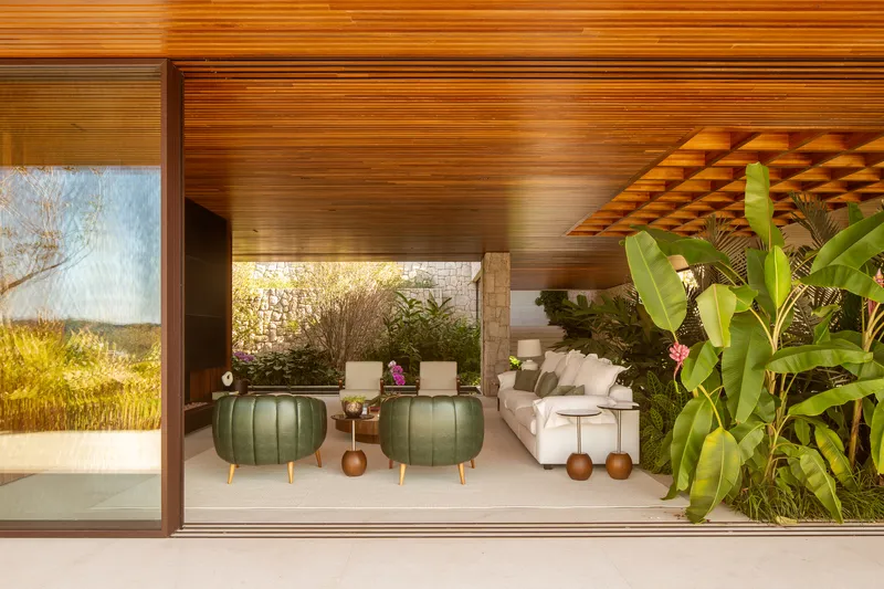 Living lounge with green leather pouffes, a low timber coffered canopy and glass walls opening to the garden