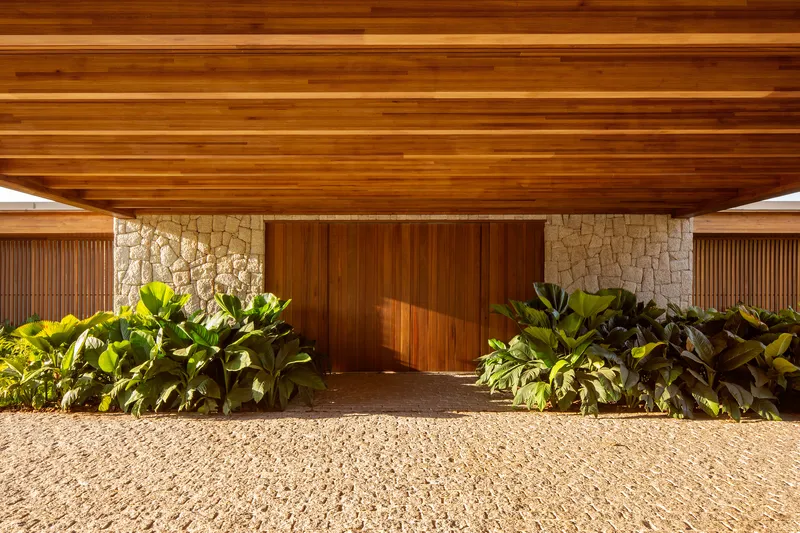 Timber-clad porte cochere with rough stone pillars and rows of planted beds at either side